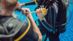Zwei Taucher in voller Tauchausrüstung üben in einem Schwimmbecken das Tauchen mit Sauerstoffflaschen.