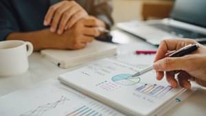 Man sieht die Hände einer Frau und eines Mannes, die einige Dokumente auf einem Tisch studieren.