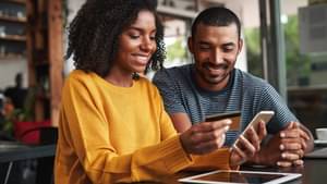 Eine Frau und ein Mann bestellen etwas online über das Smartphone und benutzen dafür ihre Kreditkarte.