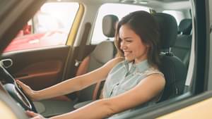 Junge Frau im ärmellosen Jeanshemd sitzt lächelnd am Steuer eines Autos.