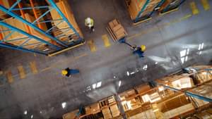 Vogelperspektive auf eine Lagerhalle in der drei Arbeiter in Schutzkleidung zu sehen sind.