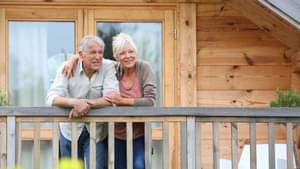 Ein Paar steht auf dem Balkon eines Ferienhauses. Die Frau legt den Arm um ihren Partner.