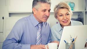 Ein älterer Mann und eine ältere Frau in Hemd und Bluse schauen auf einen Laptop