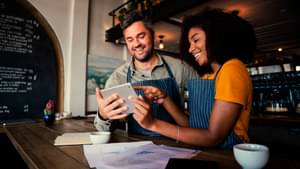 Zwei Kellner stehen in einem Café und schauen auf ein Tablet.