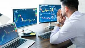 Ein junger Mann im Hemd schaut konzentriert auf zwei Monitore, die an einen Laptop angeschlossen sind.