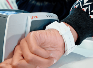 Close-Up auf ein Handgelenk mit einer Uhr, die zum Bezahlen an ein Kartenlesegerät gehalten wird