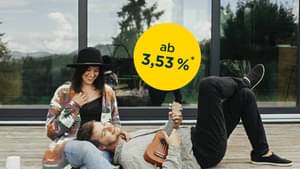 Pärchen sitzt auf einer Holzterrasse vor dessen Haus; Zinssatz ab 3,53 % p.a.*