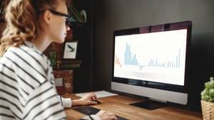 Junge Frau informiert sich am Computer über den Verlauf der Kurs-Kennzahlen