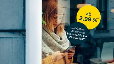 Junge Frau steht hinter bodentiefen Fenster mit Schal und gelbem Oberteil. Sie hält Handy in der Hand und tippt auf dem Bildschirm: Onlinekredit ab 2,99% p.a.* und zusätzlichen Zinsvorteil bei Online-Abschluss von bis zu 0,6% p.a.**