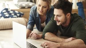 Junges Paar liegt auf dem Boden und schaut gemeinsam auf einen Laptop