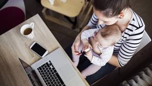 Eine Frau sitzt vor ihrem Laptop mit einem Kleinkind auf dem Schoß
