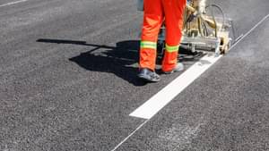 Ein Mann in einer orangenen Schutzhose ergänzt die Straßenbemalung auf einer neuen Straßendecke