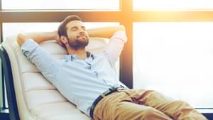 Junger Mann, der entspannt mit geschlossenen Augen auf einer Liege liegt und die Arme hinter seinem Kopf verschränkt hat