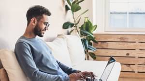 Junger Mann sitzt auf einer Couch und informiert sich über den Aktienhandel.