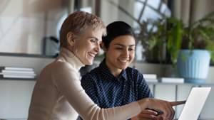 Zwei Frauen sitzen vor einem Laptop und schauen gemeinsam auf den Bildschirm.