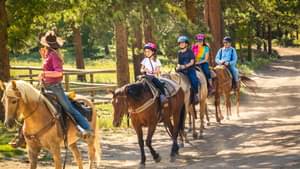 Eine Gruppe von Kindern und Jugendlichen machen eine geführte Reittour im Grünen angeführt von einer jungen Frau mit Cowboy-Hut.