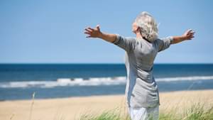 Ältere Dame steht am Meer und freut sich