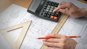 Zwei Hände, die mit einem Lineal auf einem Grundrissplan zeichnen und nebenbei Berechnungen anstellen.