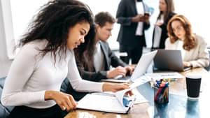Fünf junge, elegant gekleidete Menschen sitzen in einem Konferenzraum und arbeiten an ihren Laptops.