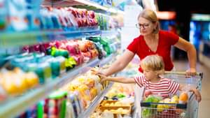 Eine Frau und ein Kind im Einkaufswagen greifen in ein bunt bepacktes Kühlregal im Supermarkt.