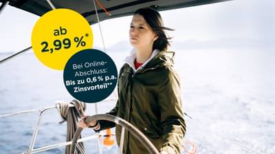 Junge Frau mit dunklen Haaren steht am Steuer eines kleinen Schiffs auf offenem Wasser: Darlehen ab 2,99% p.a.* und zusätzlichen Zinsvorteil bei Online-Abschluss von bis zu 0,6% p.a.**