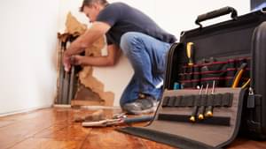 Ein Handwerker repariert Rohre in der Wand - Gebäudeversicherung