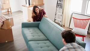 Junges Paar, das eine graue Couch durch die Wohnung trägt 