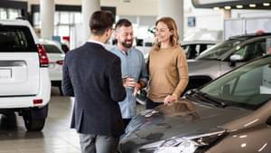Ein Verkäufer steht mit zwei Kunden in einem Autohaus.