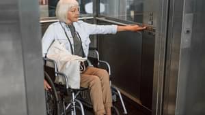 Frau im Rollstuhl im Lift drückt den Etagenknopf