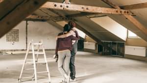 Ein Pärchen steht in einem Dachgeschoss-Rohbau und umarmt sich