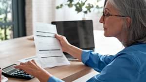 Eine Frau mit grauen Haaren und einer Brille schaut auf ein Dokument und tippt auf eine Tastatur
