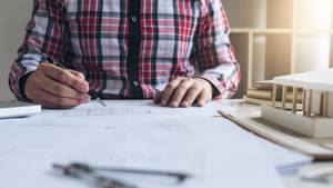 Architekt im rot karierten Hemd zeichnet in einen Bauplan.