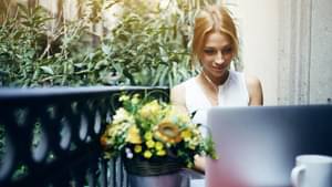 Frau sitzt draußen neben einem Geländer und arbeitet am Laptop