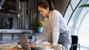 Junge Frau steht an ihrem Schreibtisch und schreibt Notizen auf Post-Its.