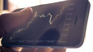 Hand hält Mobiltelefon, auf dem Aktienkurse zu sehen sind.