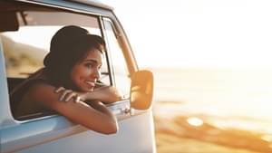 Glückliche Frau im Sommer, die sich über ihr Auto lehnt