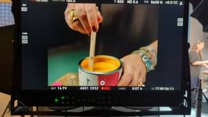 Close-Up auf eine Kamera die zeigt, wie Astrid Reintjes gelbe Farbe in einem Eimer umrührt.