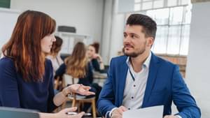 Eine junge Frau befindet sich im Beratungsgespräch mit einem jungen Mann im Anzug. Vor ihnen liegen einige Dokumente.