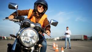 Junge Frau fährt lächelnd auf einem Übungplatz Motorrad.