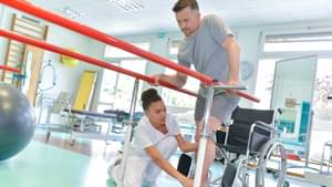 Eine Physiotherapeutin hilft einem Mann, der zuvor im Rollstuhl saß, bei Gehübungen.