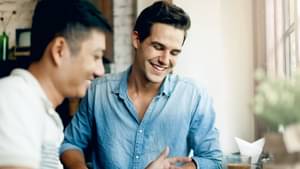 Zwei junge Männer stehen an Cafebar am Fenster und schauen auf Tablet auf dem Tisch. Einer der beiden zeigt auf den Bildschirm. 