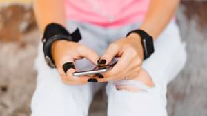 Die Hände einer jungen Frau mit schwarzem Nagellack tippen auf einem schwarzen Smartphone.